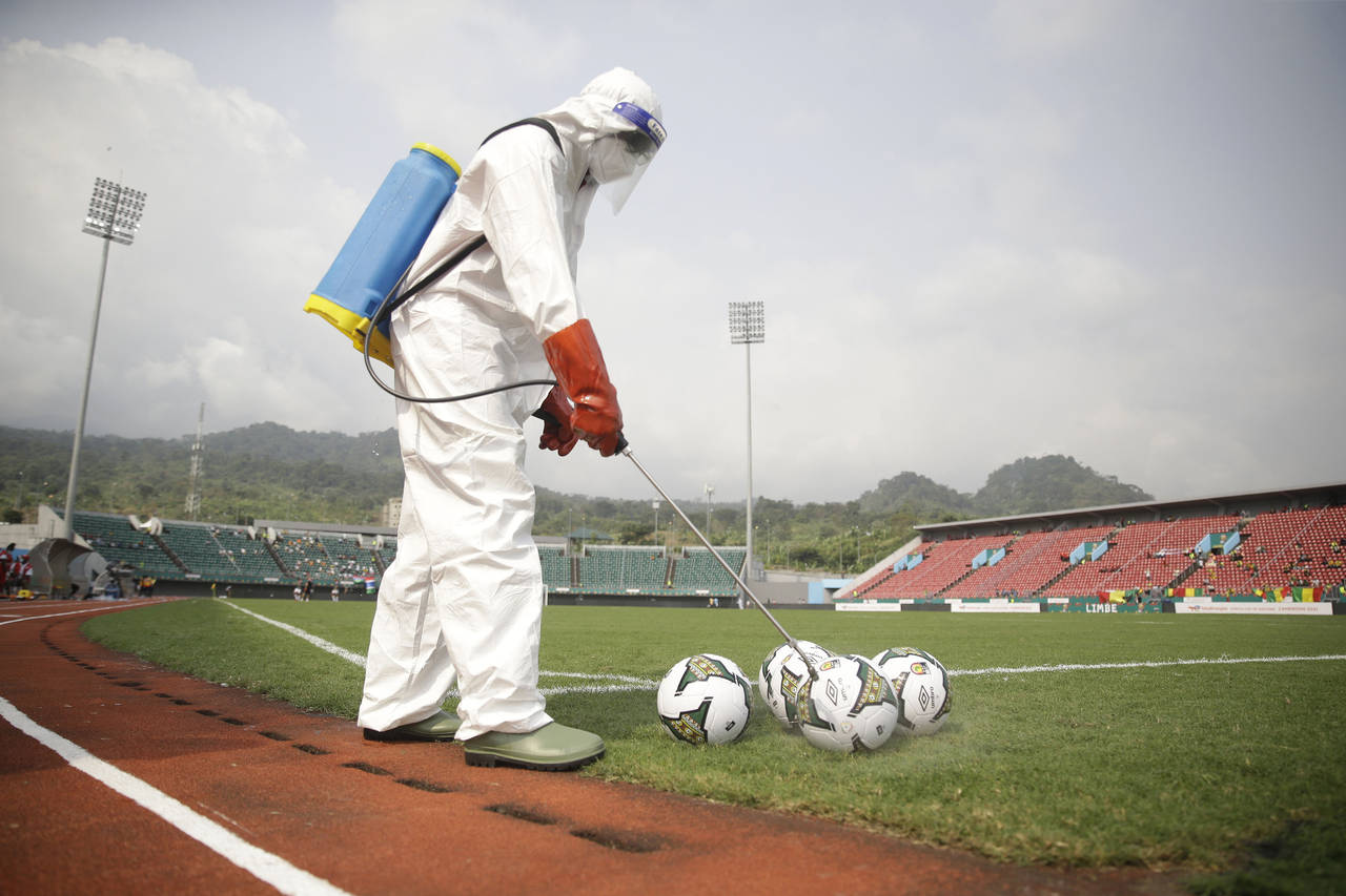 An official wearing protective gear against Covid-19 sprays soccer balls with disinfectant before t...