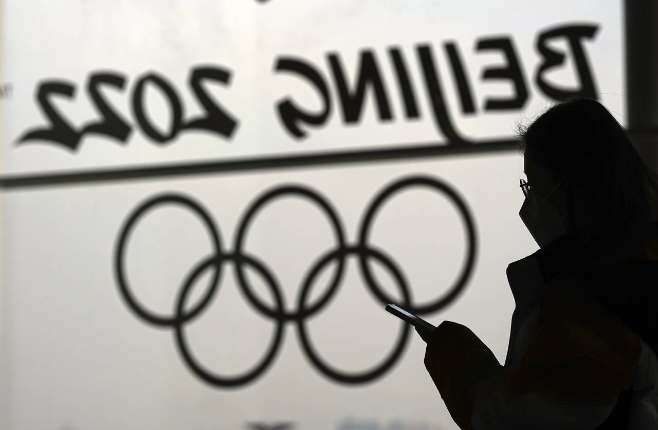FILE - A woman looks at her phone as she passes an Olympic logo inside the main media center for th...
