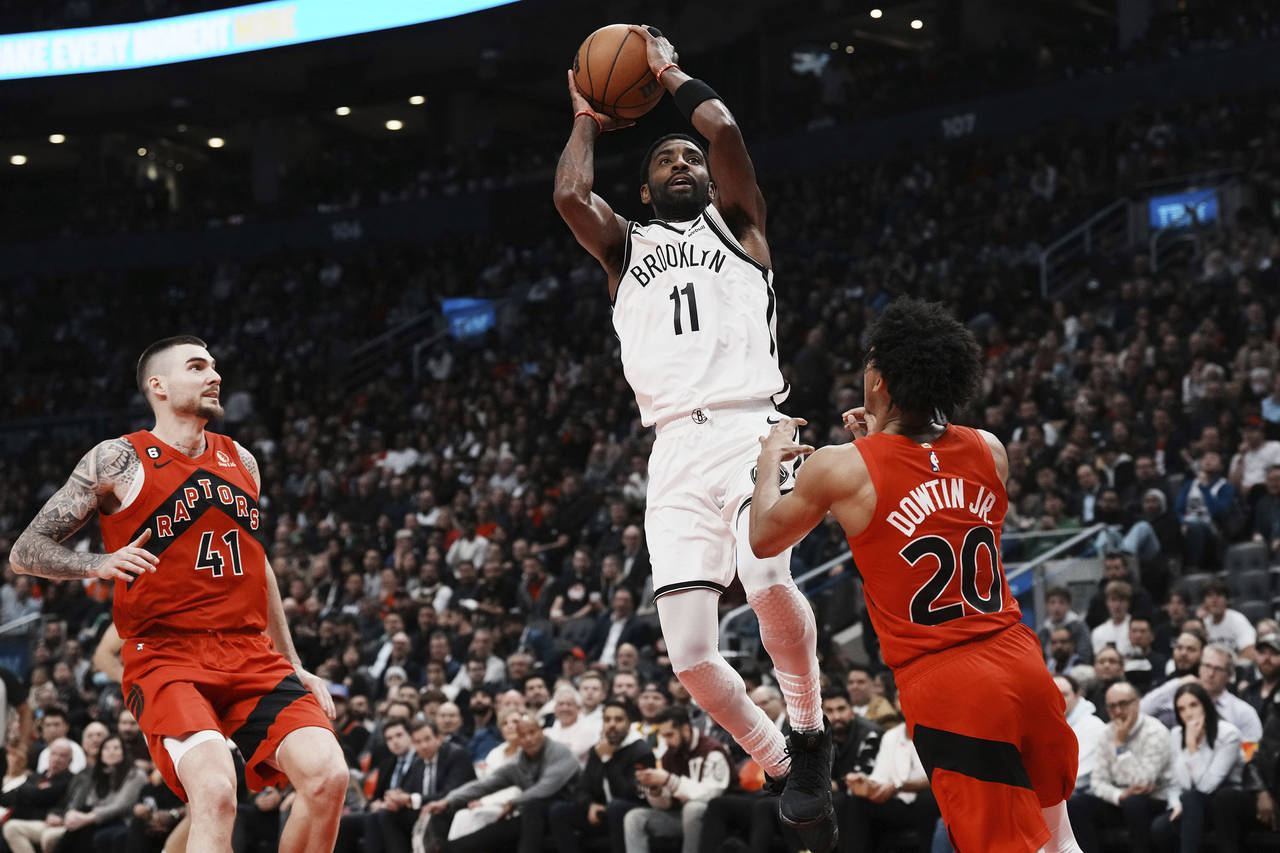 El base de los Nets de Brooklyn Kyrie Irving anota superando al base Jeff Dowtin Jr. y al alero Jua...