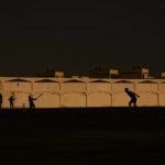 Laborers play sandlot cricket near World Cup soccer stadiums
