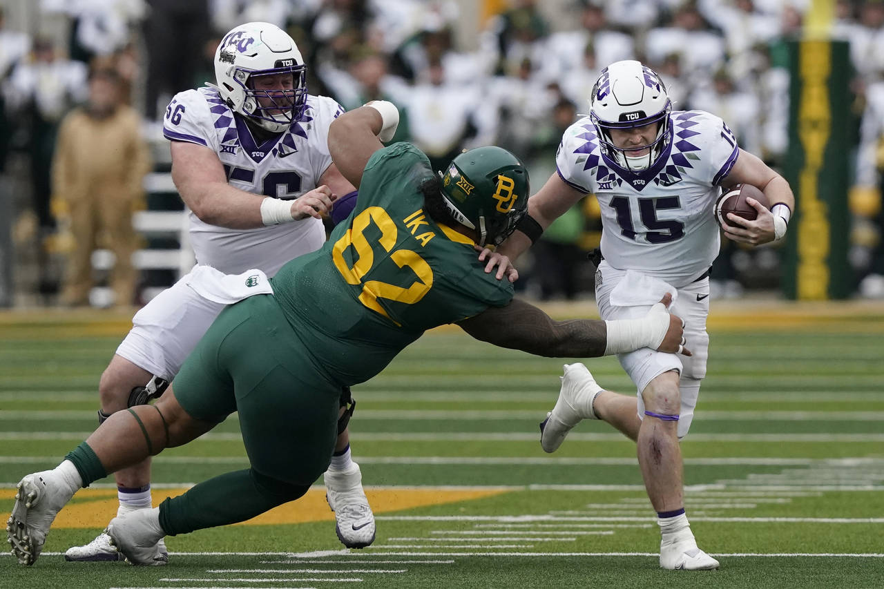 TCU quarterback Max Duggan (15) with help from teammate offensive lineman Alan Ali evades Baylor de...