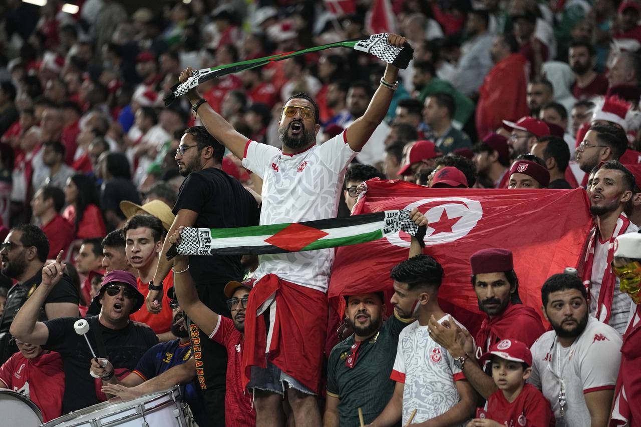 A fan holds a flag of Palestine as he cheers for the national team of Tunisia during the World Cup ...