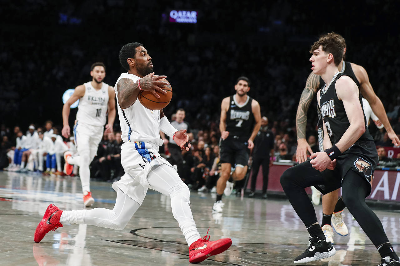 Brooklyn Nets guard Kyrie Irving, left, dribbles against Memphis Grizzlies forward Jake LaRavia (3)...