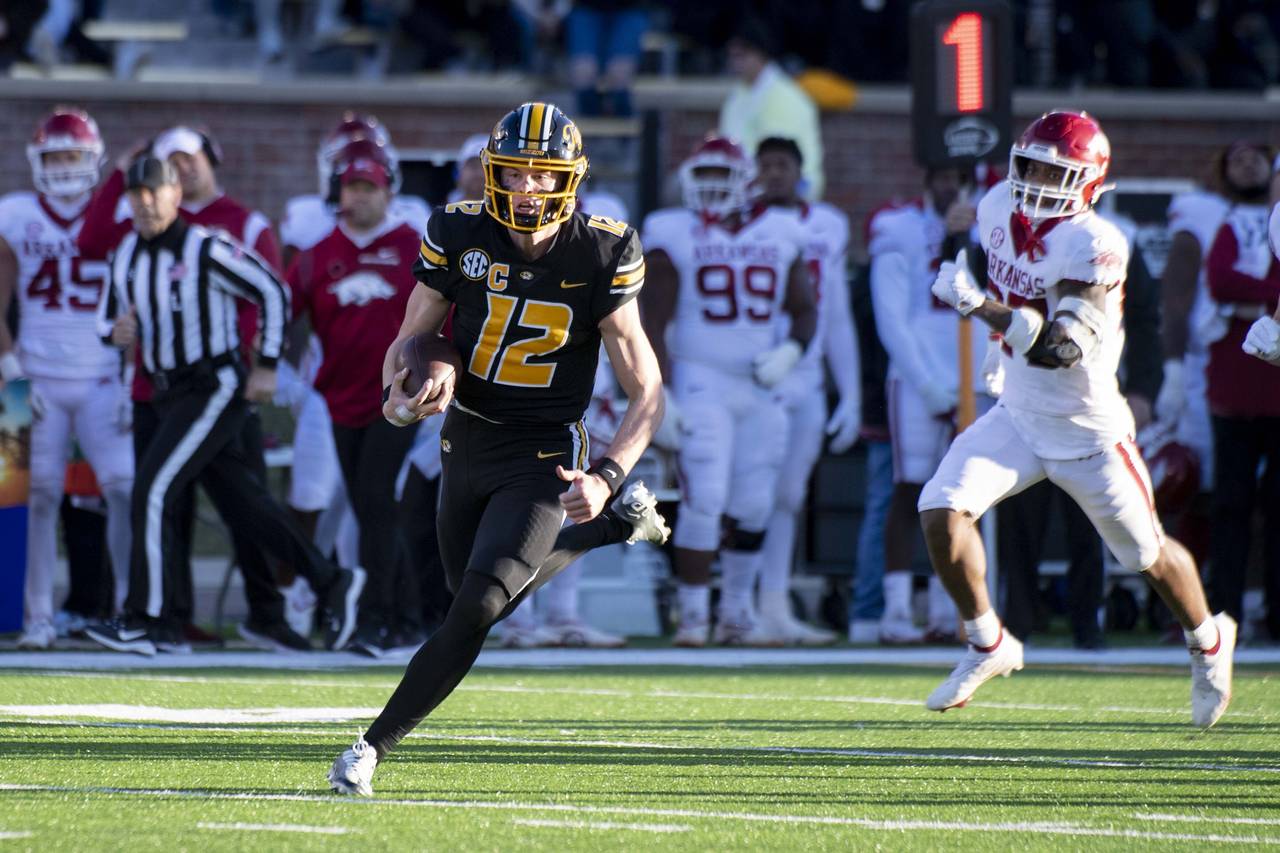 Missouri quarterback Brady Cook, left, runs past Arkansas linebacker Chris Paul Jr., right, during ...