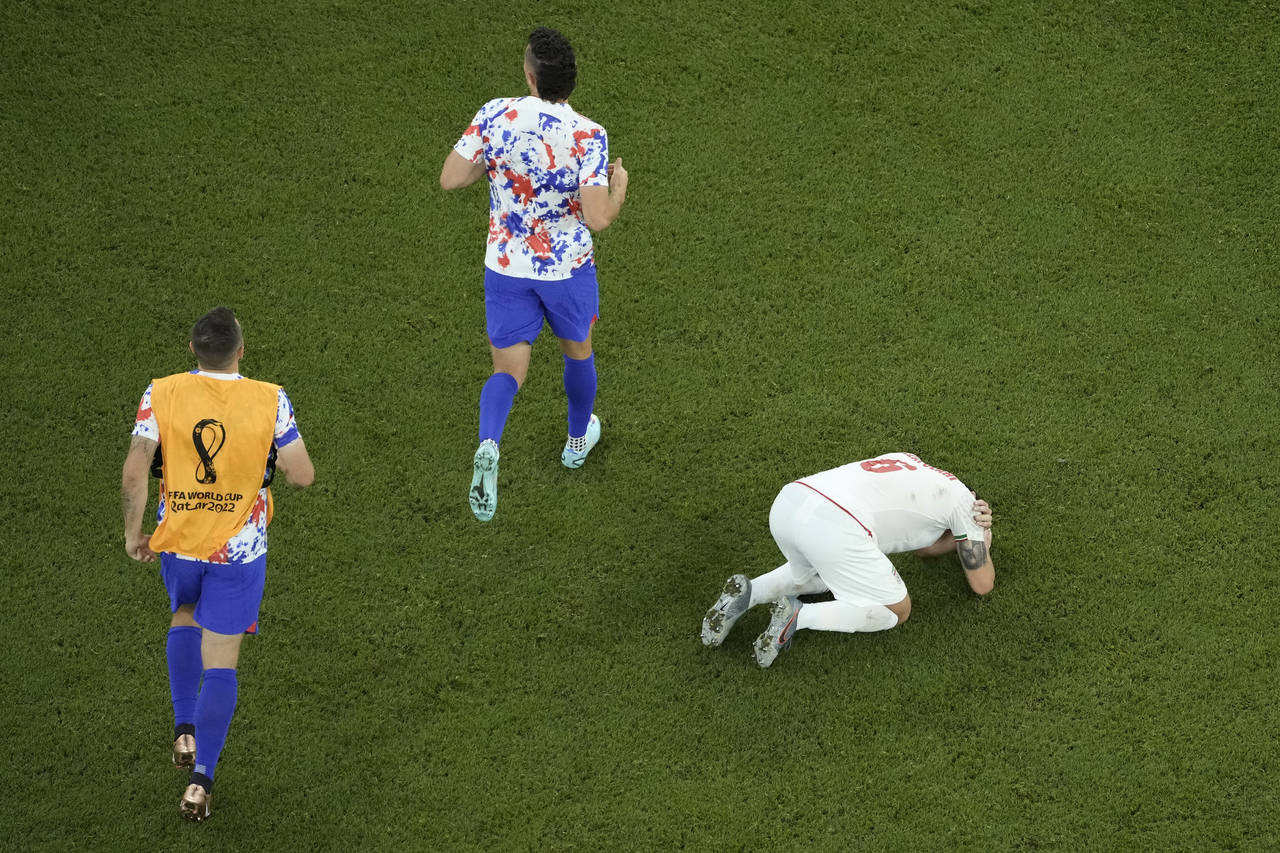 Iran's Saeid Ezatolahi, right, reacts while the players of the United States celebrate at the end o...