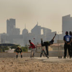 Laborers play sandlot cricket near World Cup soccer stadiums