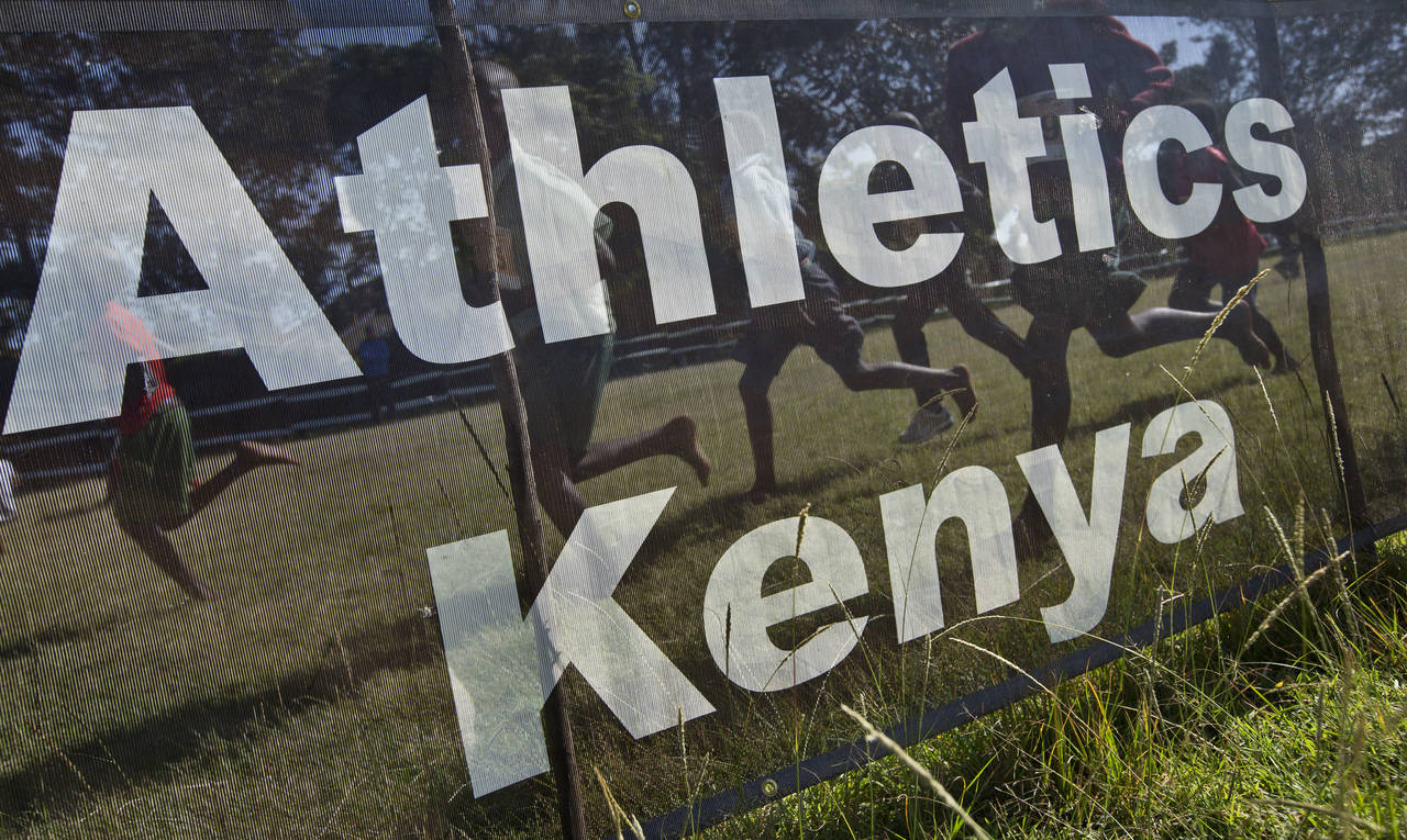FILE - Junior athletes run past a sign for Athletics Kenya at the Discovery cross country races, an...