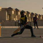 Laborers play sandlot cricket near World Cup soccer stadiums