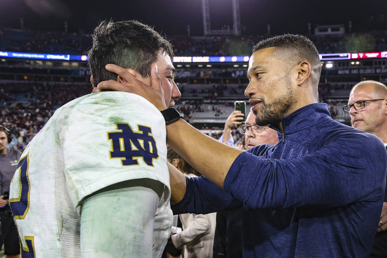 Notre Dame quarterback Tyler Buchner, left, and head coach Marcus Freeman, right, embrace on the fi...