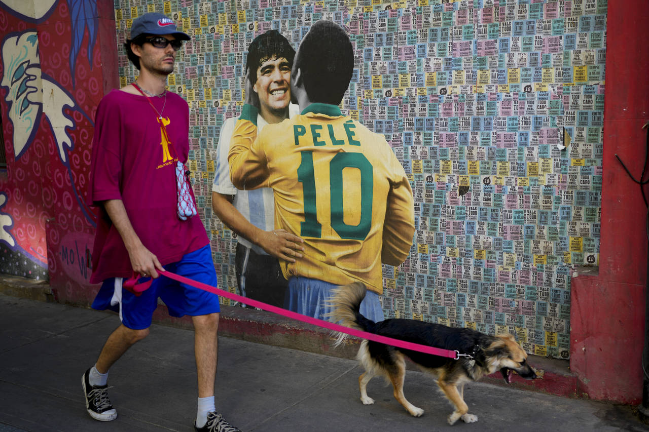 A man walks his dog walk past a mural showing Brazilian soccer legend Pele and Argentina late socce...