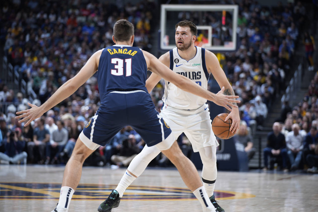 El jugador de los Mavericks de Dallas Luka Doncic, al fondo, es defendido por el jugador de los Nug...