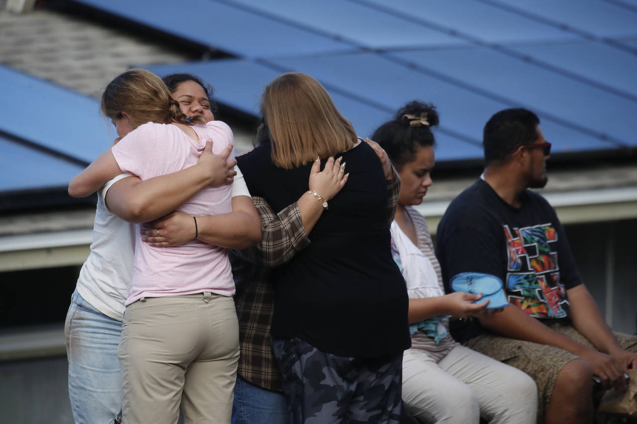 People embrace on a street in Kailua, where at least a man died and a few others were seriously inj...