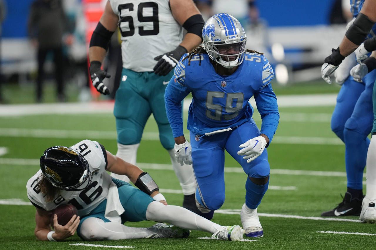 Jacksonville Jaguars quarterback Trevor Lawrence holds his left leg after being sacked by Detroit L...