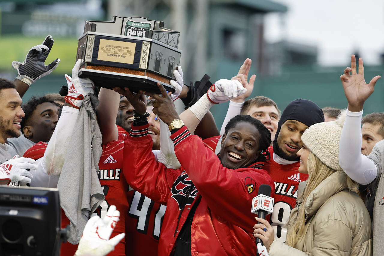 Louisville head coach Deion Branch holds up the trophy as his players celebrate around him after th...