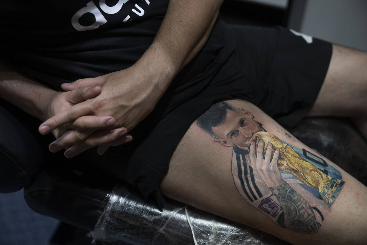 Sebastian Fernandez rests as artist César "Yeyo" Molina tattoos his leg with an image of soccer p...