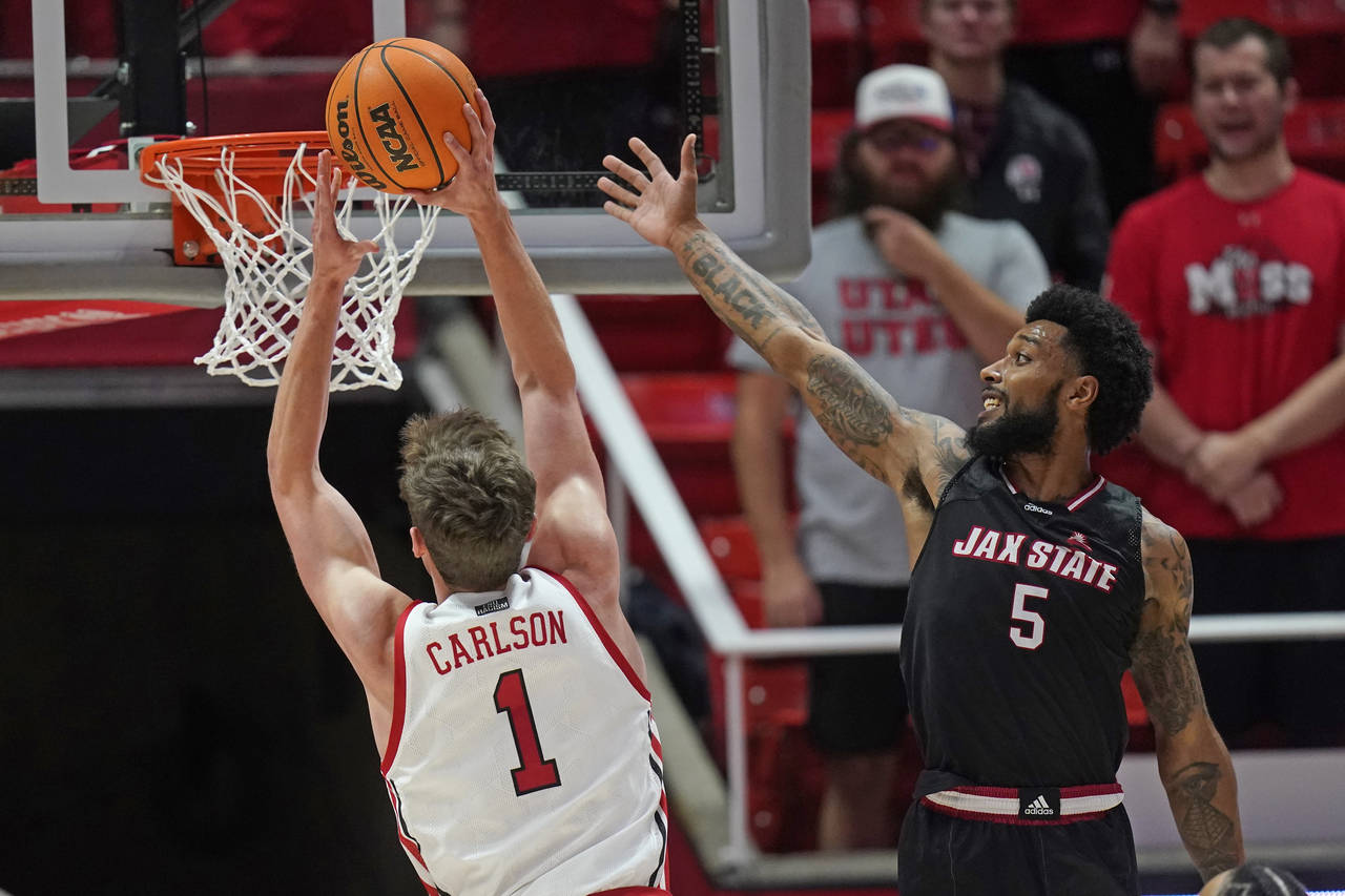 Utah forward Ben Carlson (1) goes to the basket as Jacksonville State guard Skyelar Potter (5) defe...