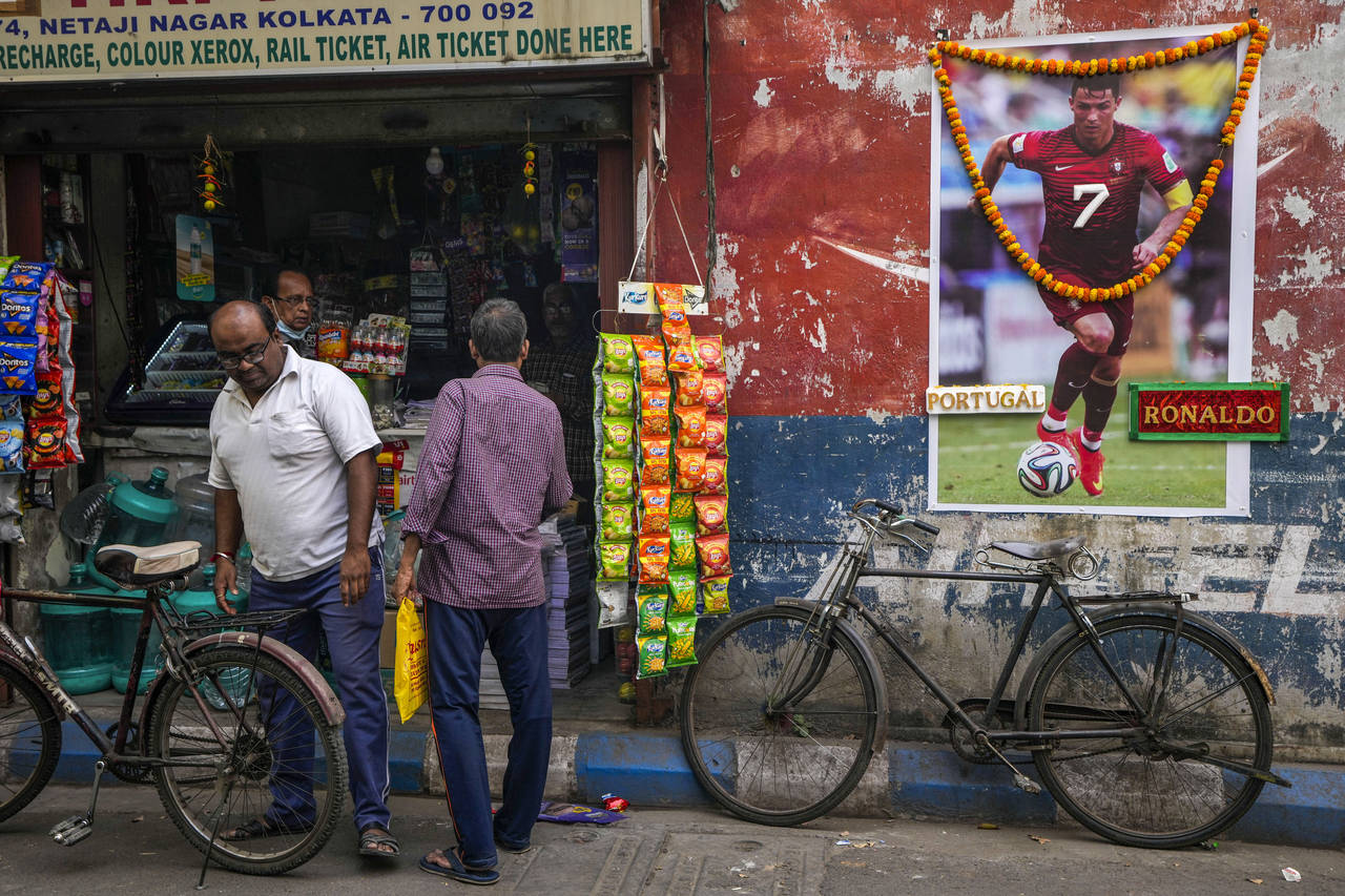 People buy grocery from a shop next to a garlanded photograph of Portugal's Cristiano Ronaldo put u...