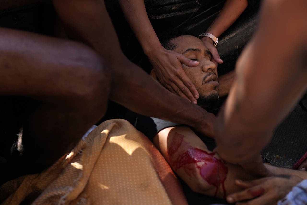 A resident comforts a wounded man as he is placed in the back of a truck after a police operation t...
