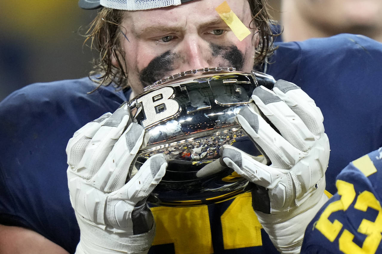 Michigan linebacker Kechaun Bennett kisses the trophy as he celebrates with teammates after defeati...