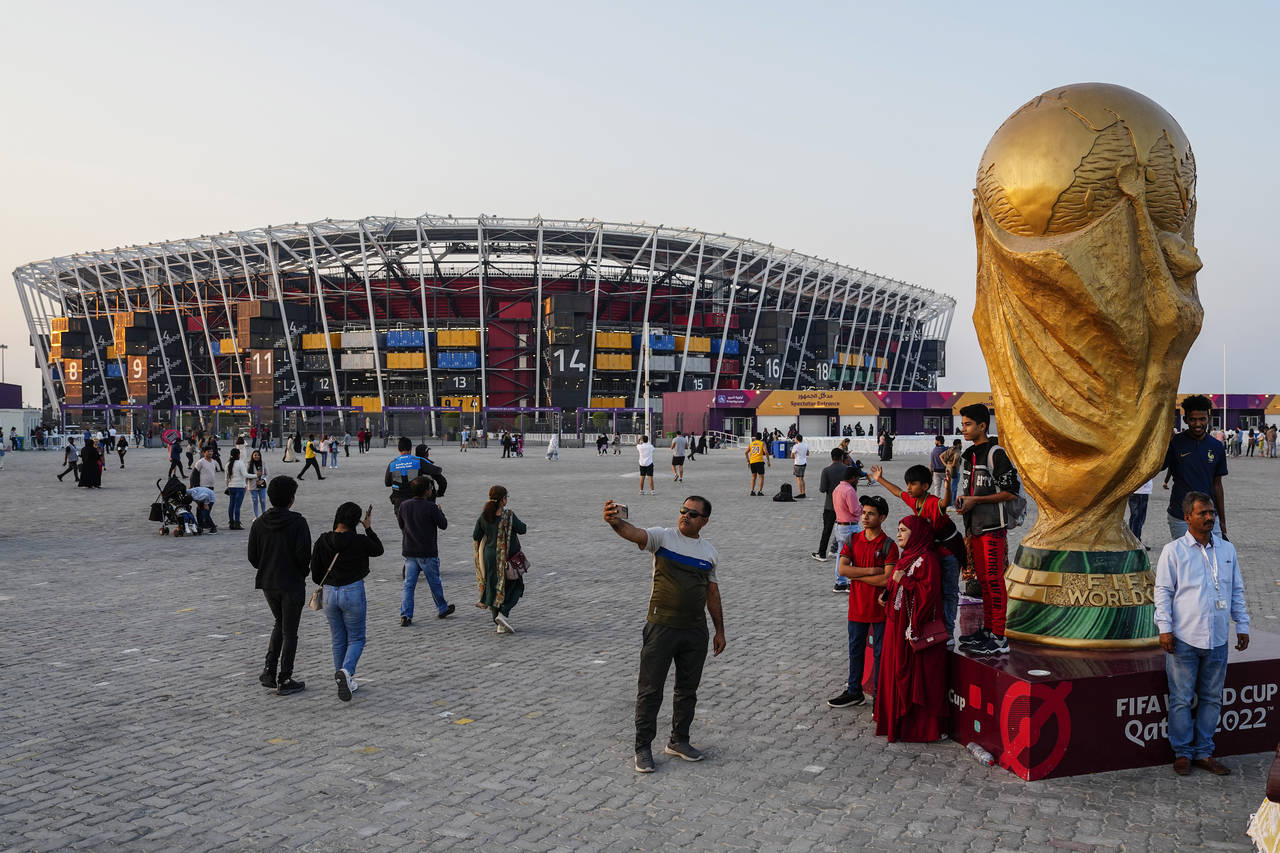 People pose for pictures next to a replica of the World Cup Trophy, right, with the Stadium 974 in ...