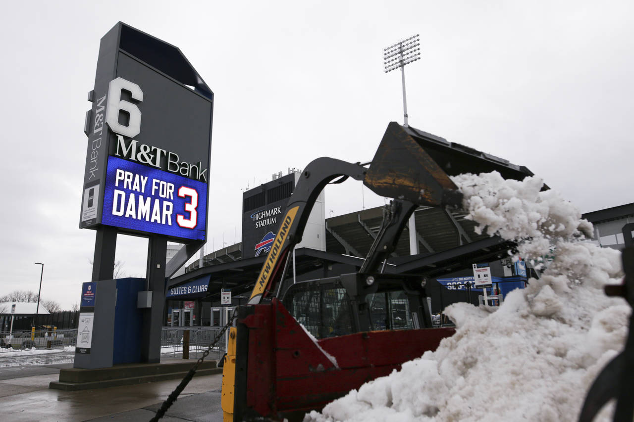 Crews clear snow from a parking lot near a sign showing support for Buffalo Bills safety Damar Haml...
