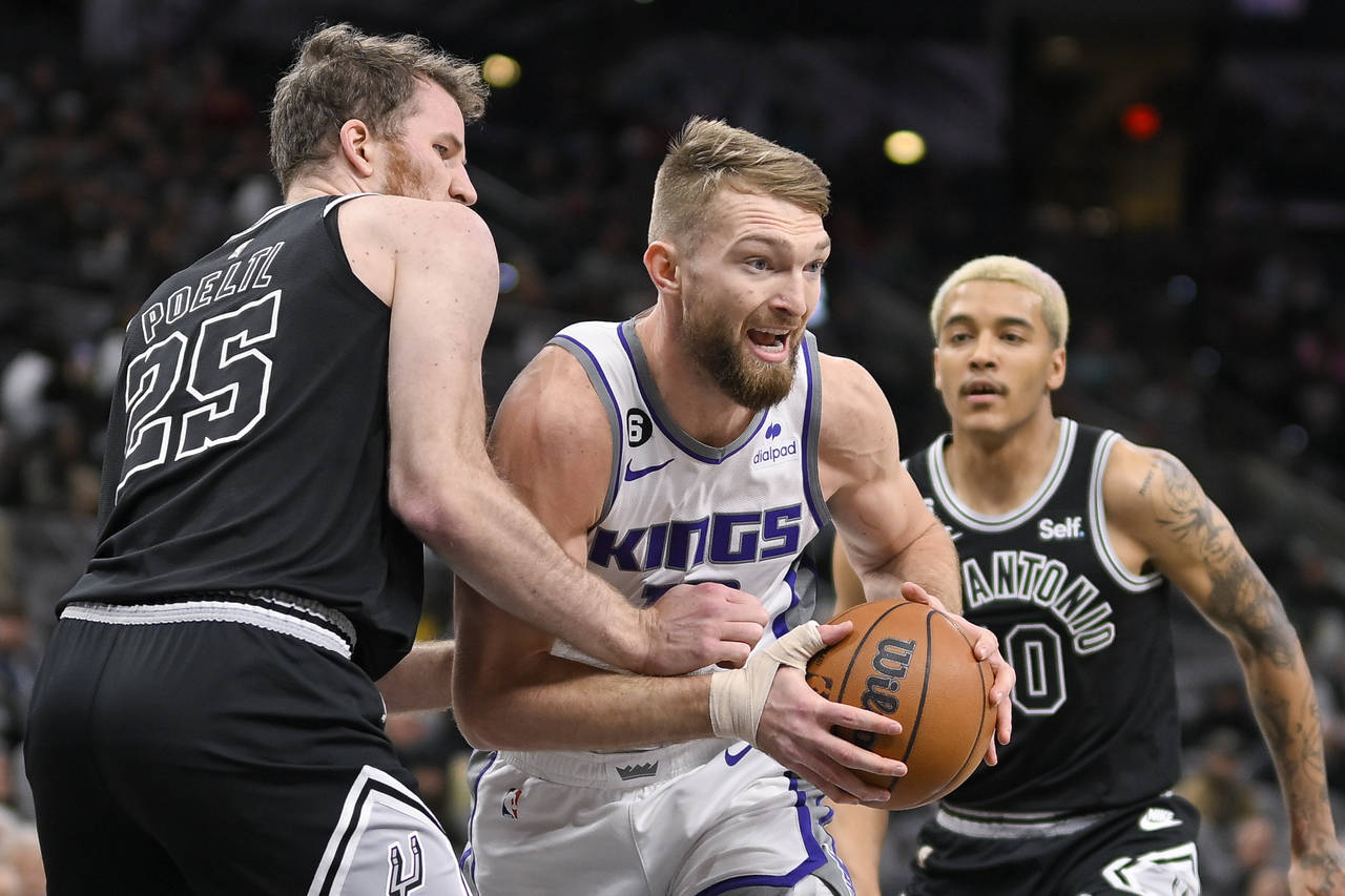 Sacramento Kings' Domantas Sabonis, center, drives between San Antonio Spurs' Jakob Poeltl (25) and...