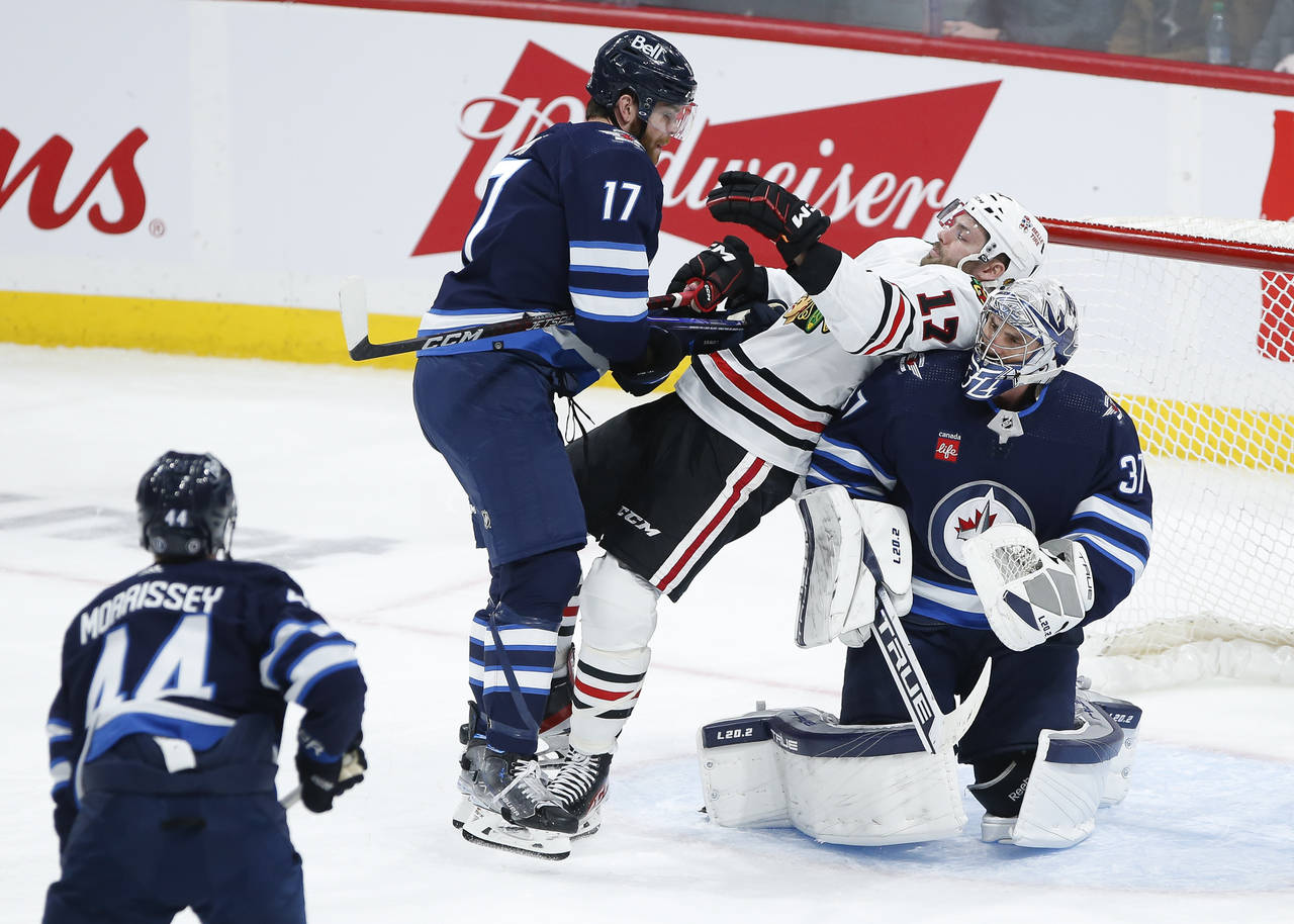Winnipeg Jets' Adam Lowry (17) pushes Chicago Blackhawks' Jason Dickinson (17) against goaltender C...