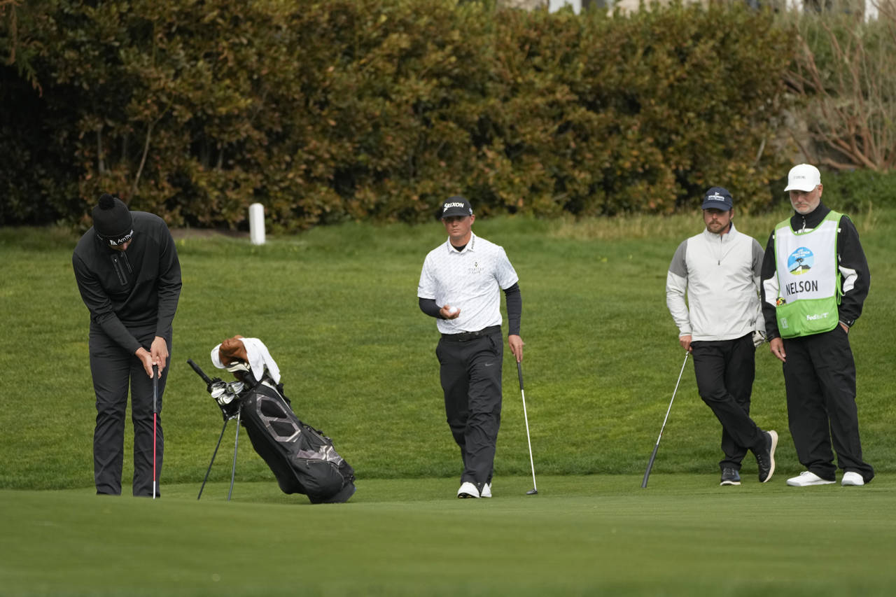 Beau Hossler, left, putts on the 13th green of the Pebble Beach Golf Links as Max McGreevy, center,...